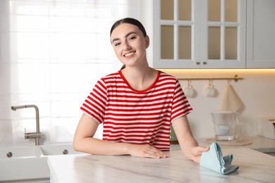 Photo of Beautiful young woman cleaning white marble table with rag in kitchen