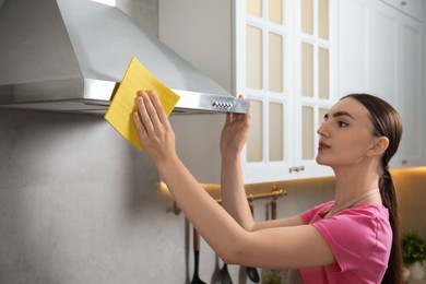 Beautiful young woman cleaning kitchen hood with napkin at home