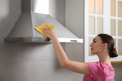 Beautiful young woman cleaning kitchen hood with napkin at home