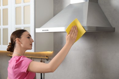 Beautiful young woman cleaning kitchen hood with napkin at home