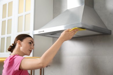 Beautiful young woman cleaning kitchen hood with napkin at home