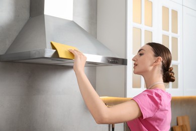 Photo of Beautiful young woman cleaning kitchen hood with napkin at home