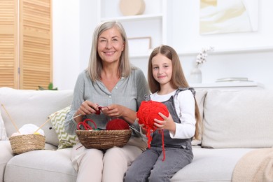 Happy grandmother with granddaughter holding knitting needles and yarn on sofa at home