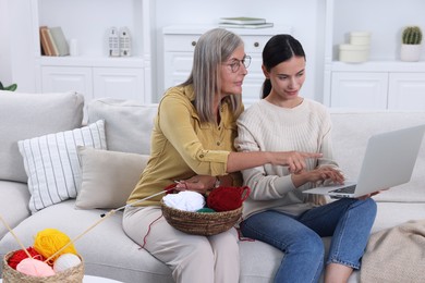 Photo of Mother and daughter watching video tutorial via laptop how to knit on sofa at home