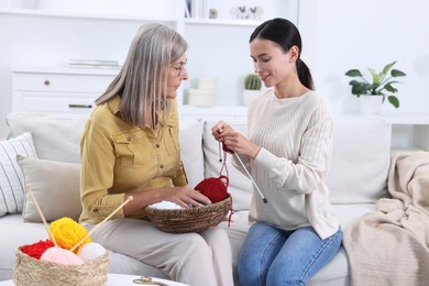 Mother observing her daughter knitting on sofa at home