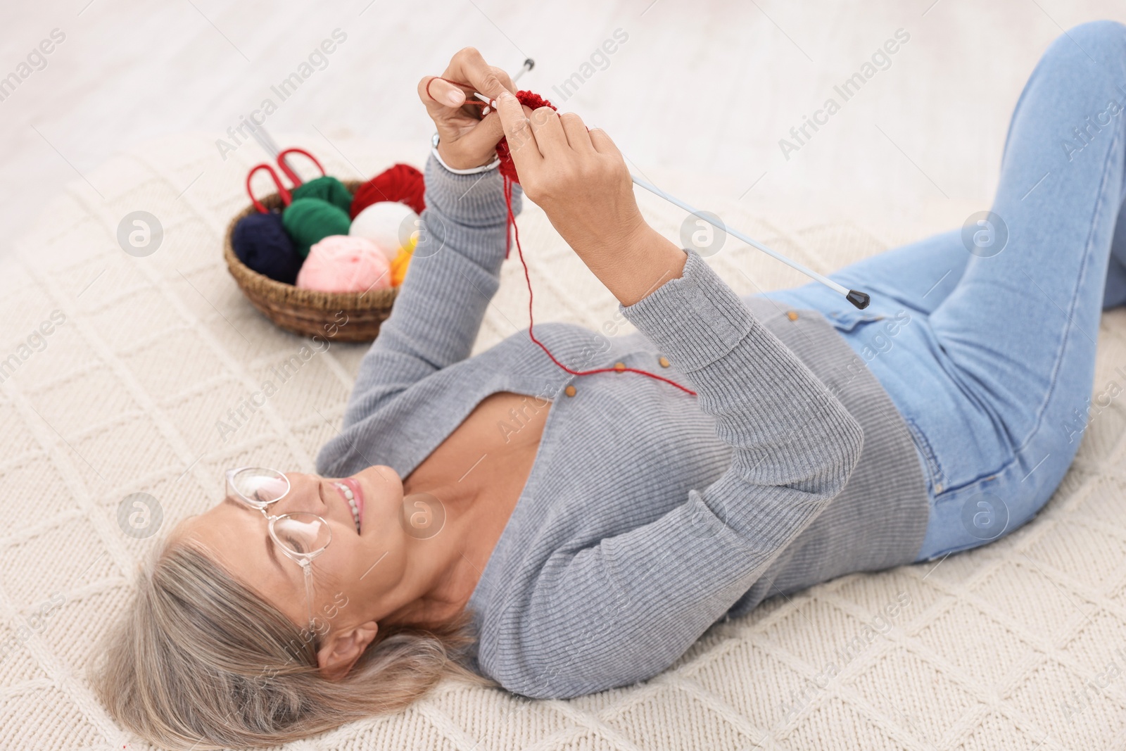 Photo of Smiling senior woman knitting on bed at home