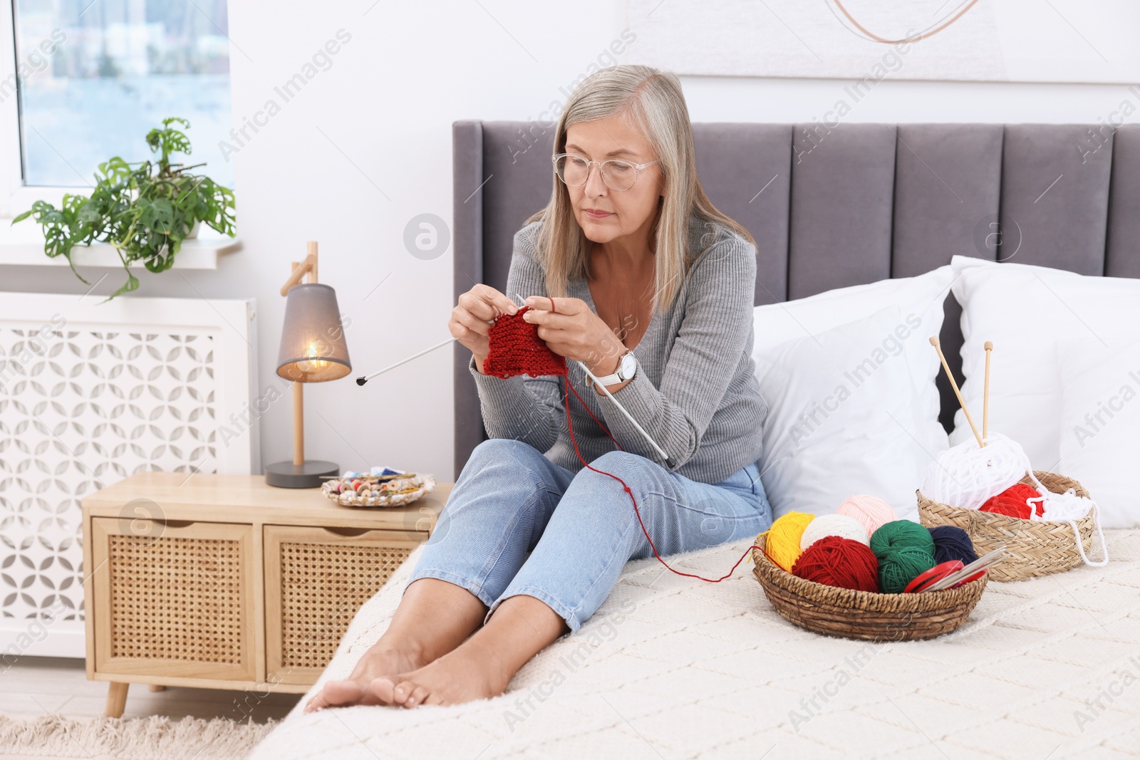 Photo of Beautiful senior woman knitting on bed at home