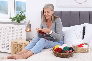 Beautiful senior woman knitting on bed at home