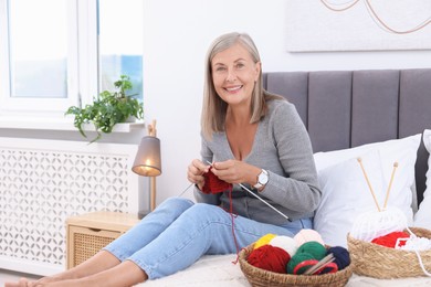 Smiling senior woman knitting on bed at home