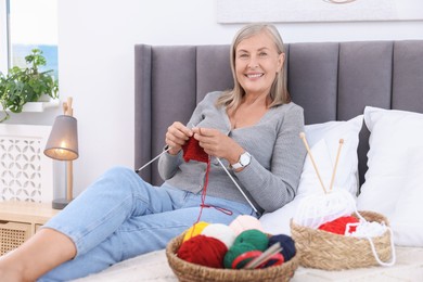 Smiling senior woman knitting on bed at home