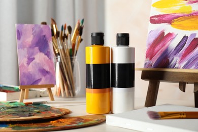 Photo of Acrylic paints of different colors, small easels, palettes and brushes on light table indoors