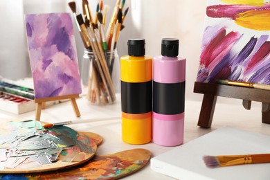 Photo of Acrylic paints of different colors, small easels, palettes and brushes on wooden table indoors