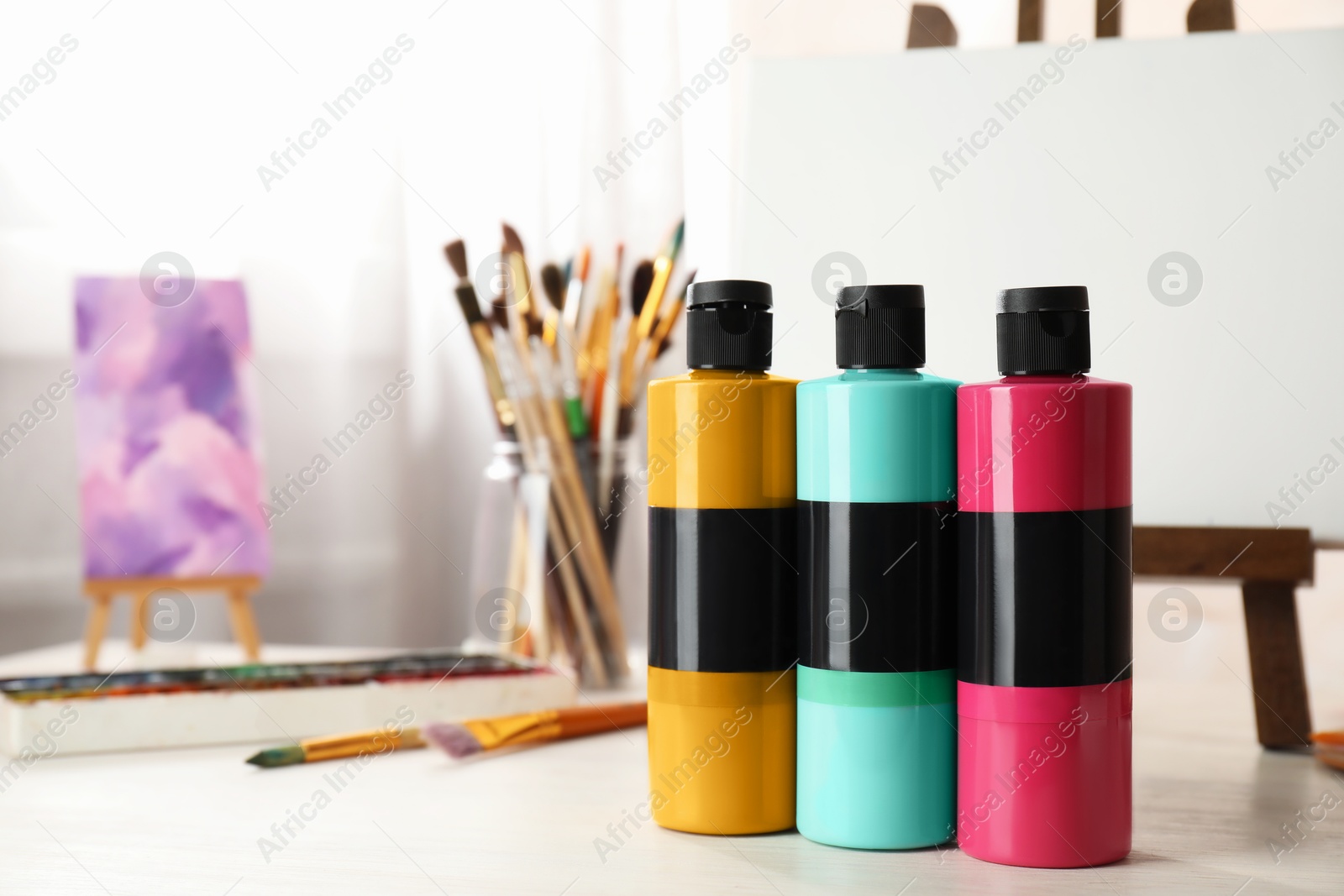 Photo of Acrylic paints of different colors, small easels, palette and brushes on wooden table indoors