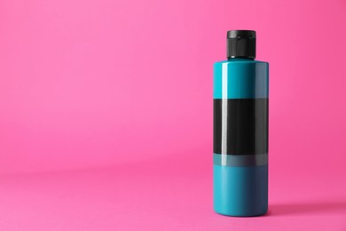 Photo of Turquoise acrylic paint in bottle on pink background, space for text