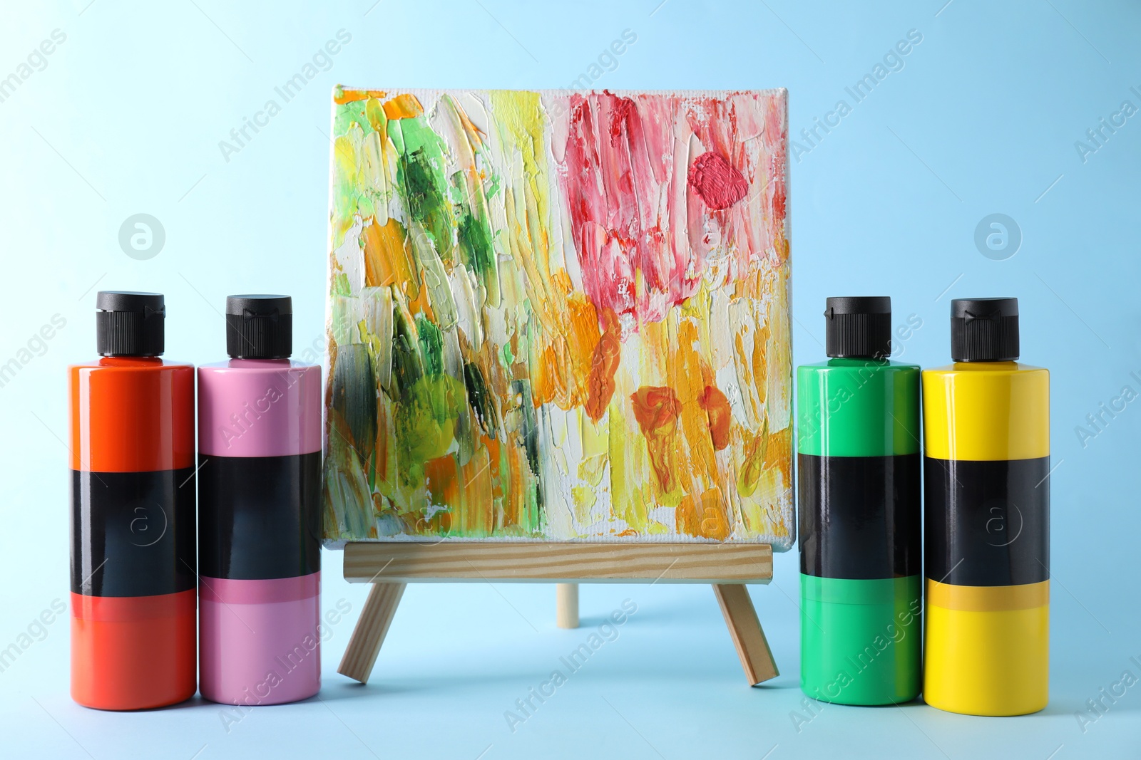 Photo of Acrylic paints of different colors and small easel with abstract picture on light blue background