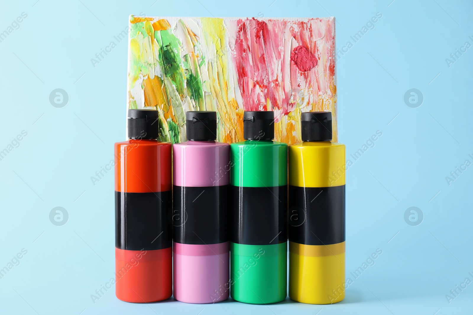 Photo of Acrylic paints of different colors and small easel with abstract picture on light blue background