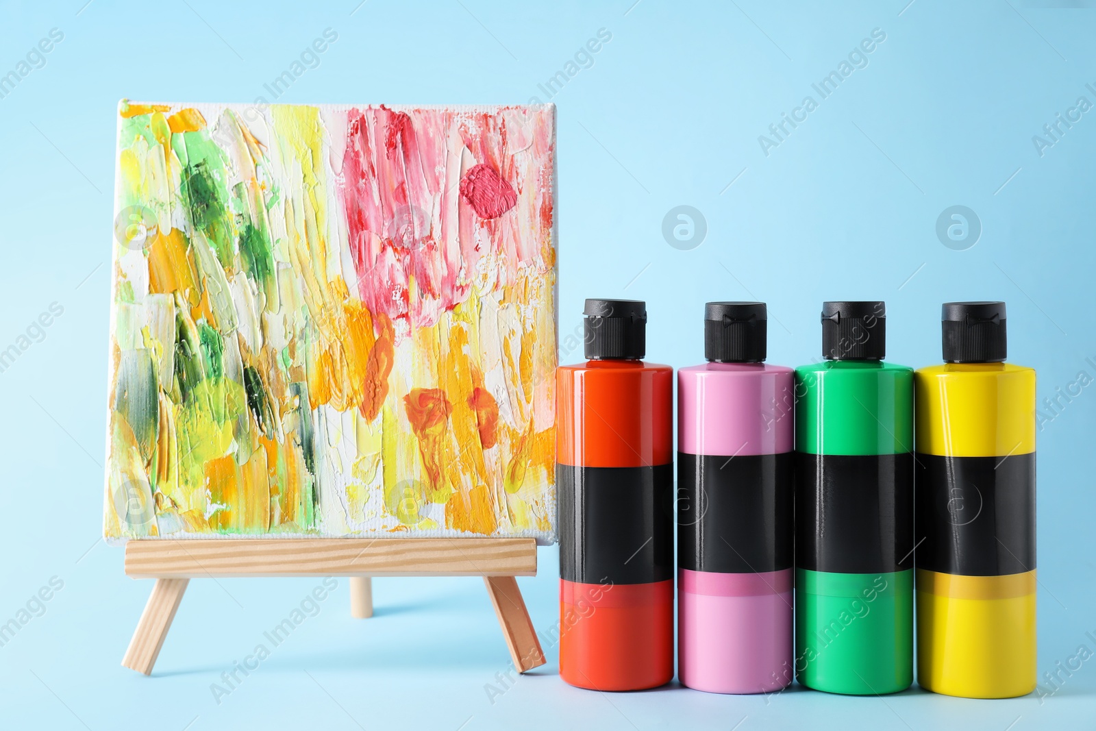 Photo of Acrylic paints of different colors and small easel with abstract picture on light blue background