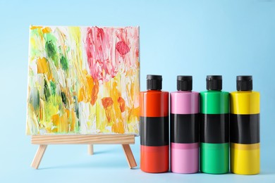 Photo of Acrylic paints of different colors and small easel with abstract picture on light blue background