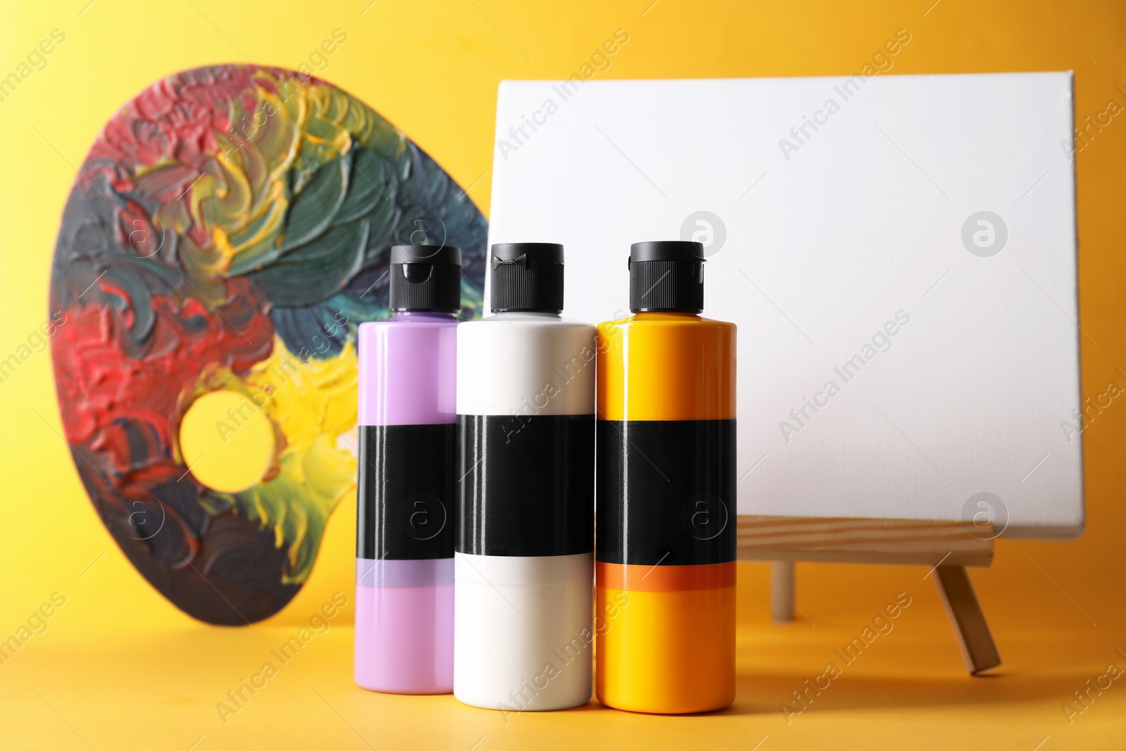 Photo of Acrylic paints of different colors, palette and small easel on orange background