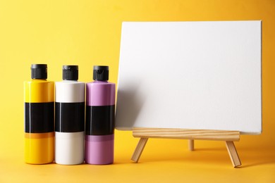 Photo of Acrylic paints of different colors and small easel on orange background