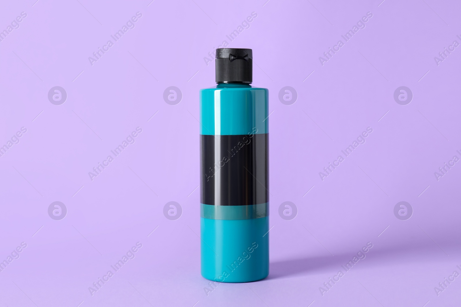 Photo of Turquoise acrylic paint in bottle on violet background