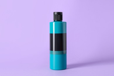 Photo of Turquoise acrylic paint in bottle on violet background