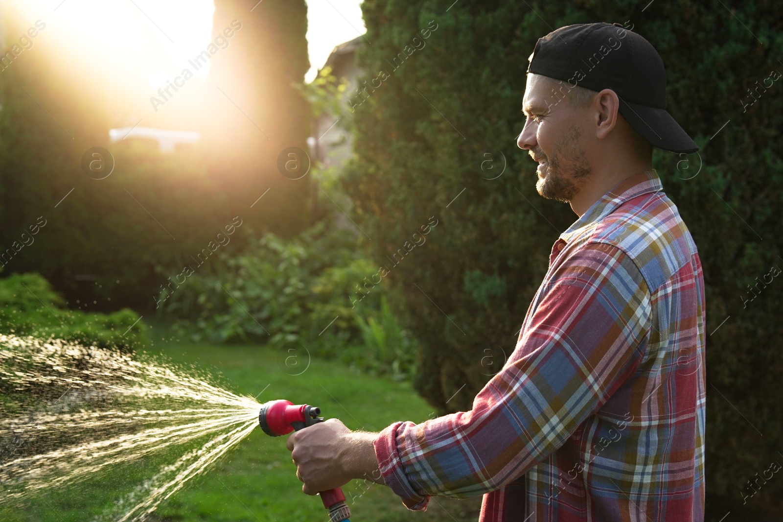 Photo of Man watering lawn with hose in backyard