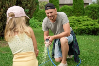 Father and his daughter watering lawn with hose in backyard, selective focus