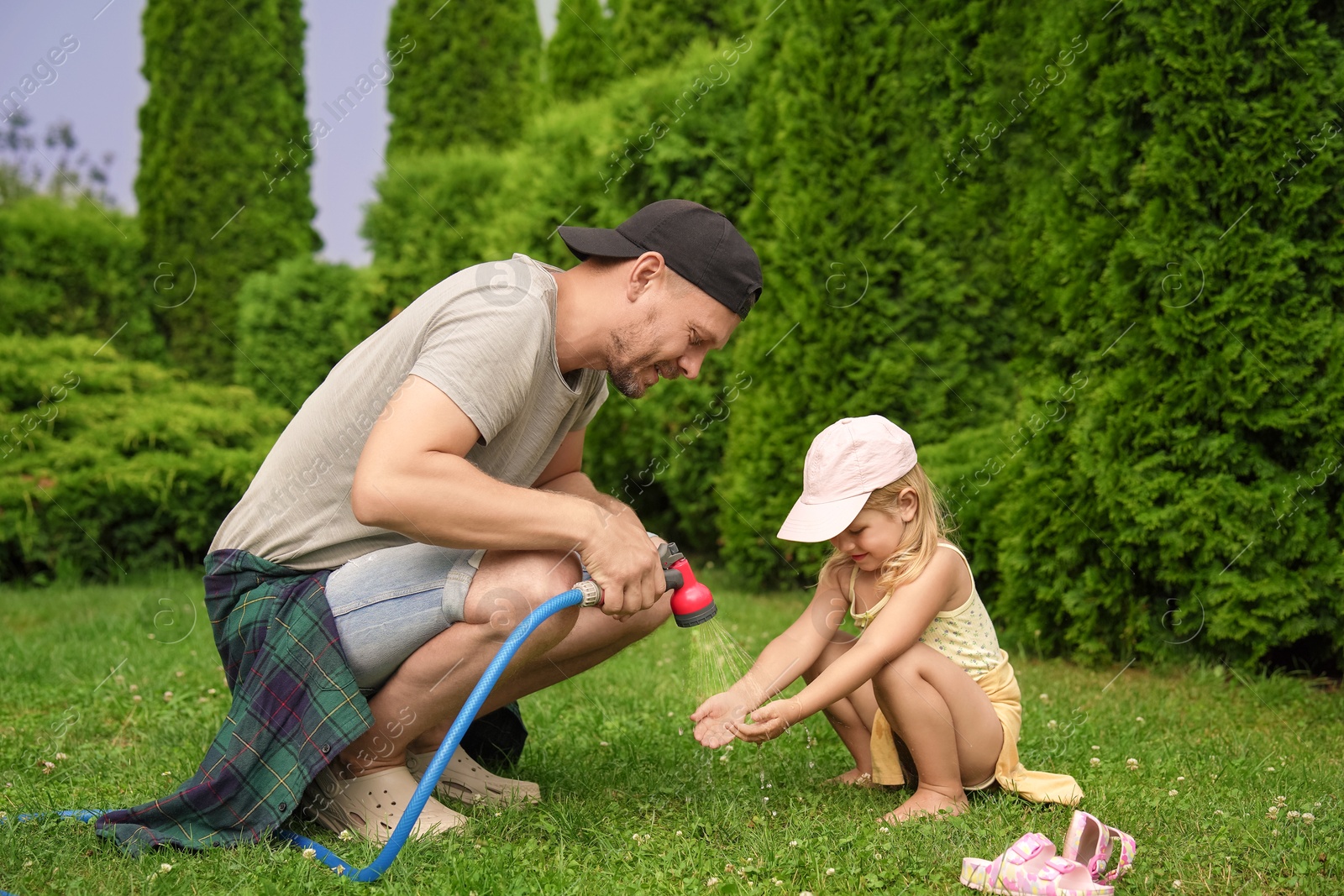 Photo of Father with hose spraying water and his daughter on lawn in backyard