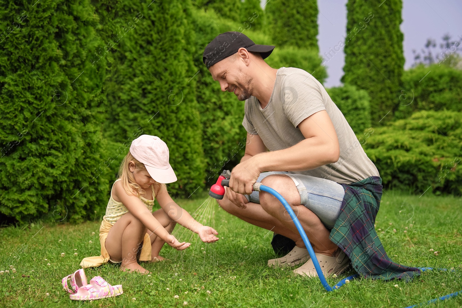 Photo of Father with hose spraying water and his daughter on lawn in backyard