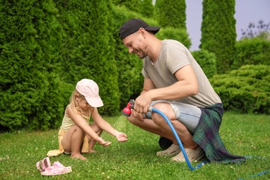 Photo of Father with hose spraying water and his daughter on lawn in backyard