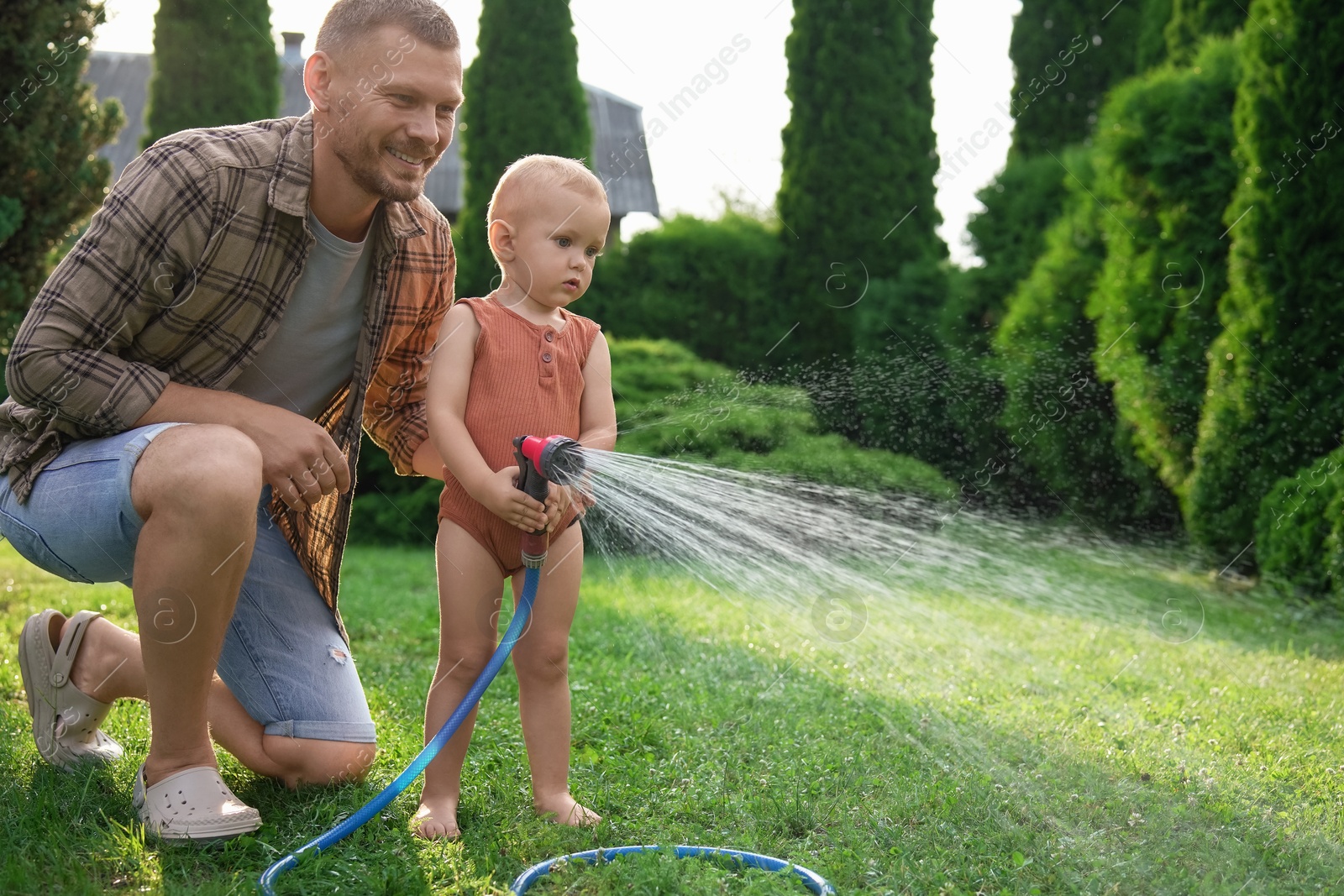 Photo of Father and his son watering lawn with hose in backyard