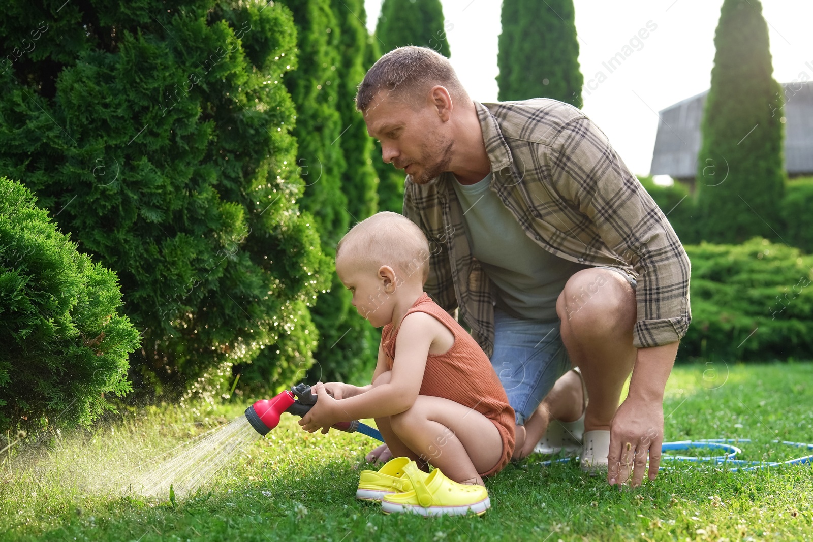 Photo of Father and his son watering lawn with hose in backyard