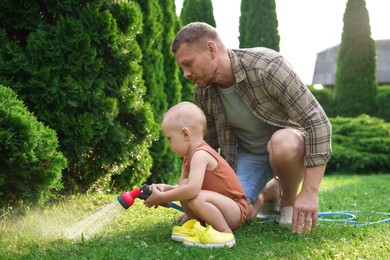 Father and his son watering lawn with hose in backyard