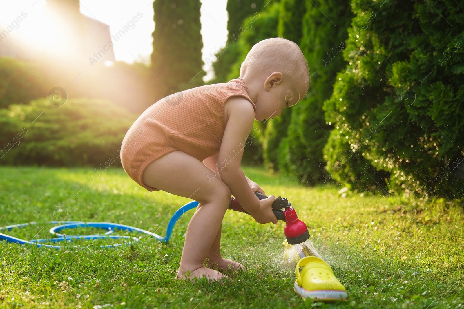 Photo of Little boy with hose on green lawn in backyard