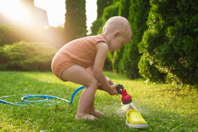 Little boy with hose on green lawn in backyard