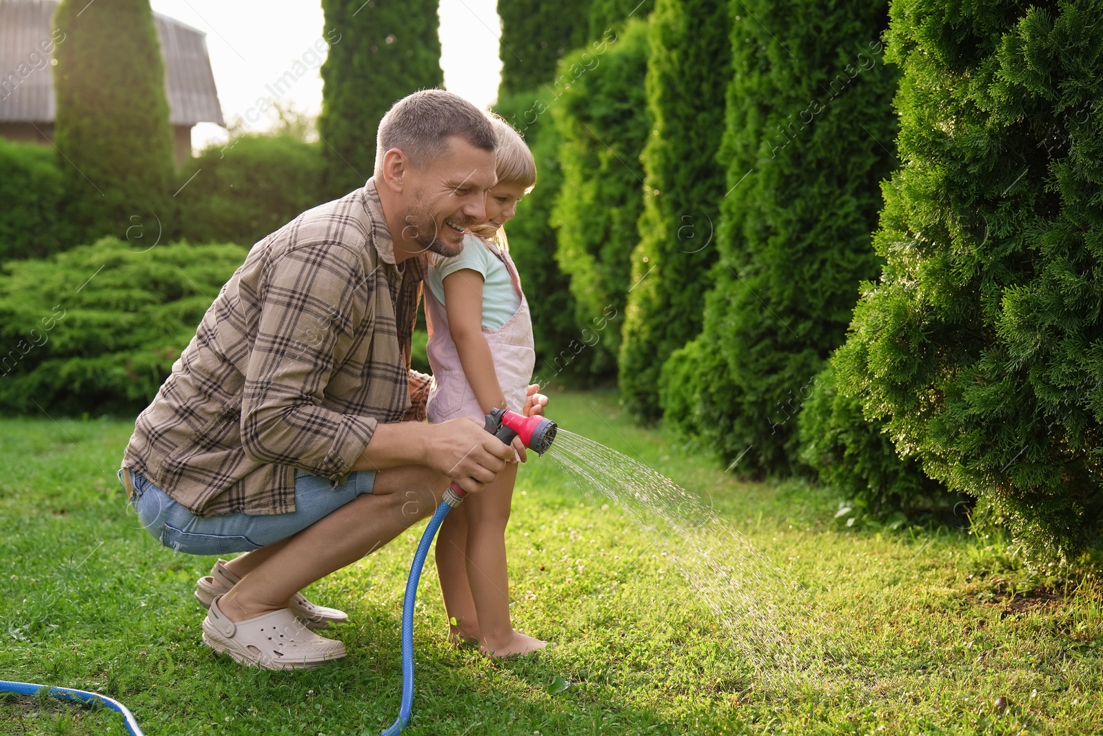 Photo of Little girl and her father watering lawn with hose in backyard