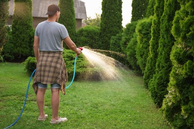 Man watering lawn with hose in backyard, back view