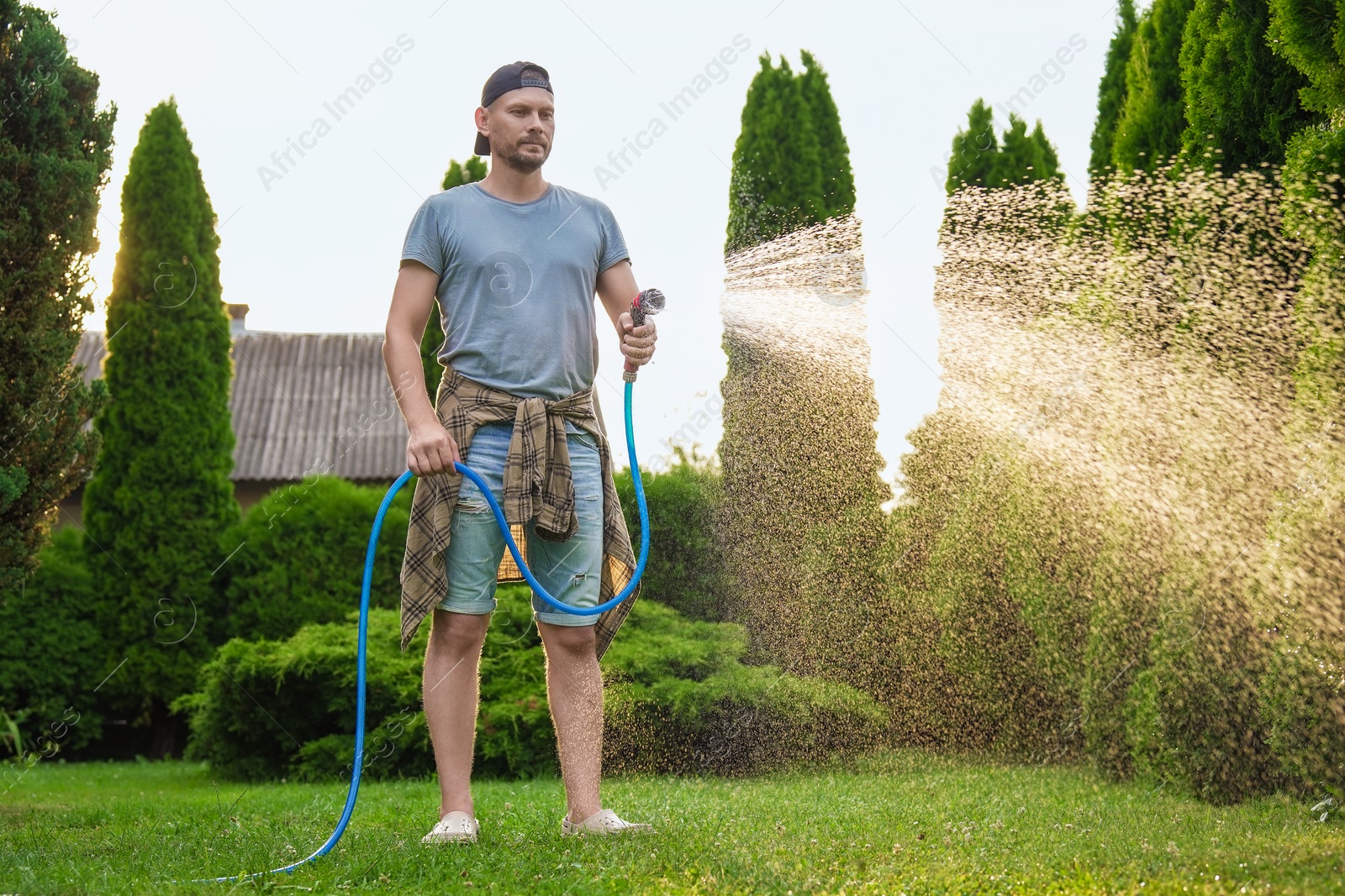 Photo of Man watering lawn with hose in backyard, low angle view