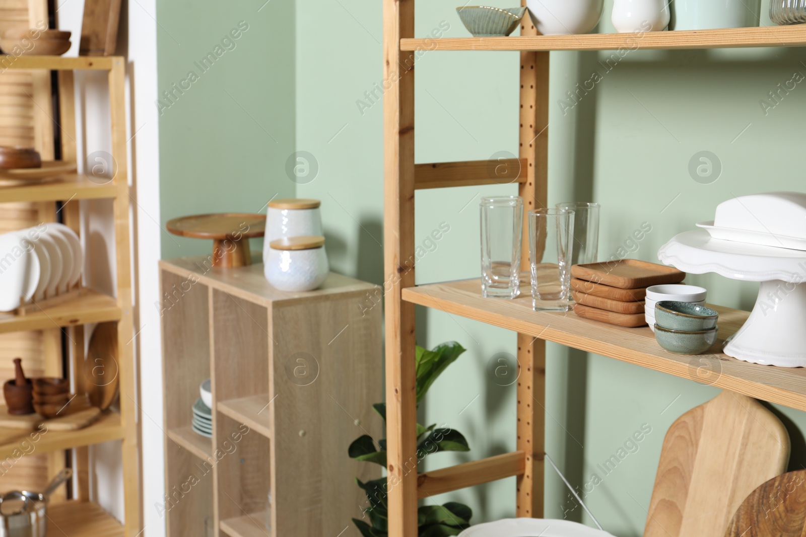 Photo of Wooden storage stands and shelving unit with kitchenware near green wall indoors