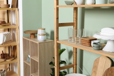 Wooden storage stands and shelving unit with kitchenware near green wall indoors