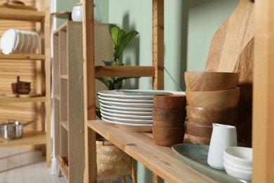 Photo of Wooden storage stands with kitchenware near green wall indoors, closeup