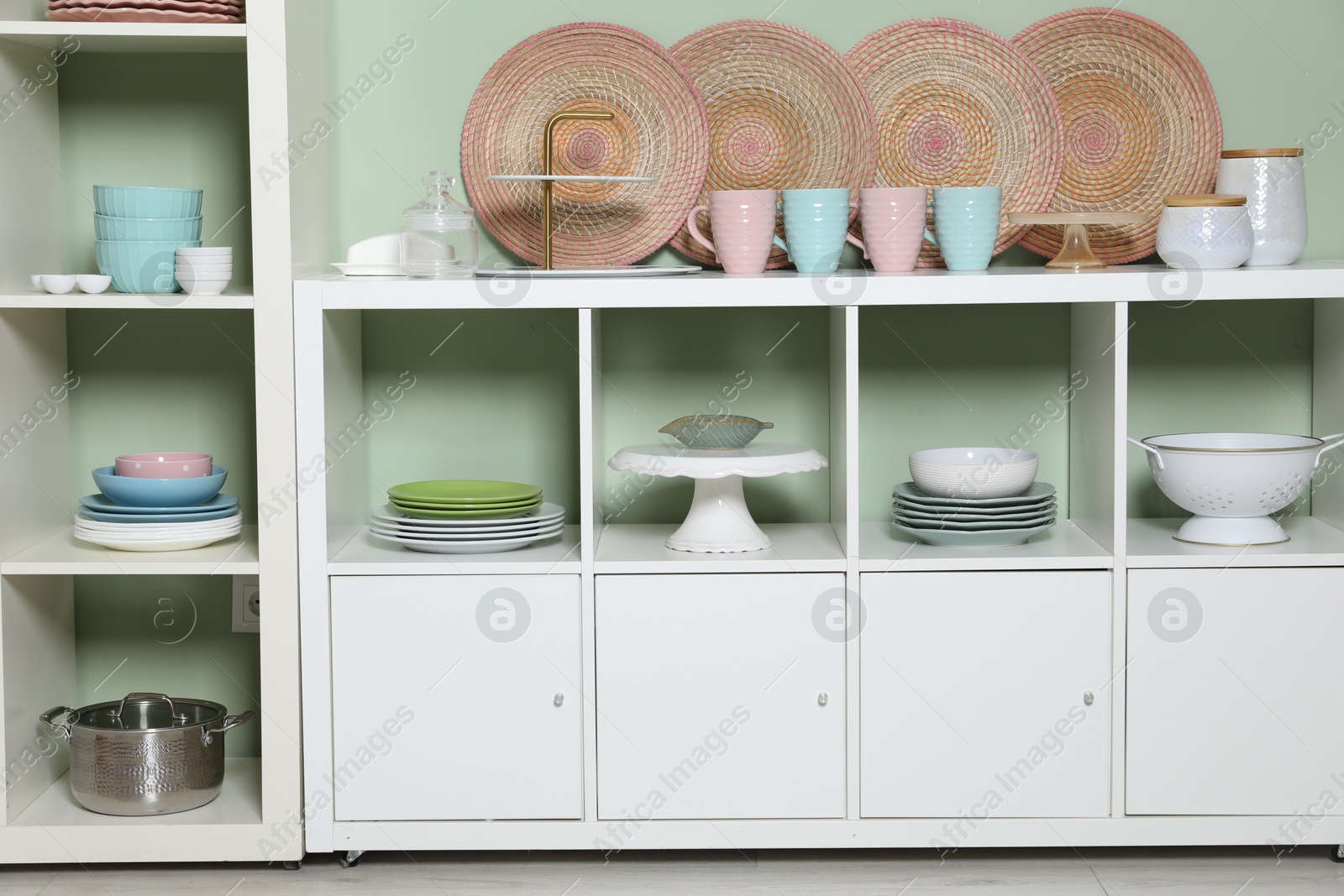 Photo of Shelving unit and storage cabinet with kitchenware near green wall