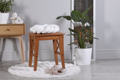 Wooden stool with knot cushion in room. Stylish interior design