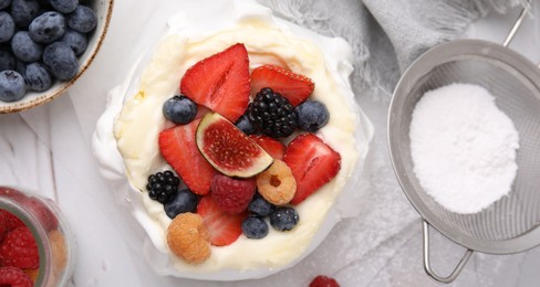 Photo of Pavlova cake (meringue dessert) with whipped cream, fresh berries, fig and powdered sugar on table, top view