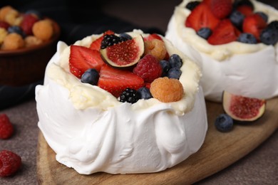 Photo of Pavlova cake (meringue dessert) with whipped cream, fresh berries and fig on brown table, closeup