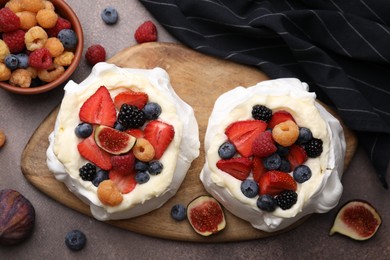 Photo of Pavlova cake (meringue dessert) with whipped cream, fresh berries and fig on brown table, flat lay