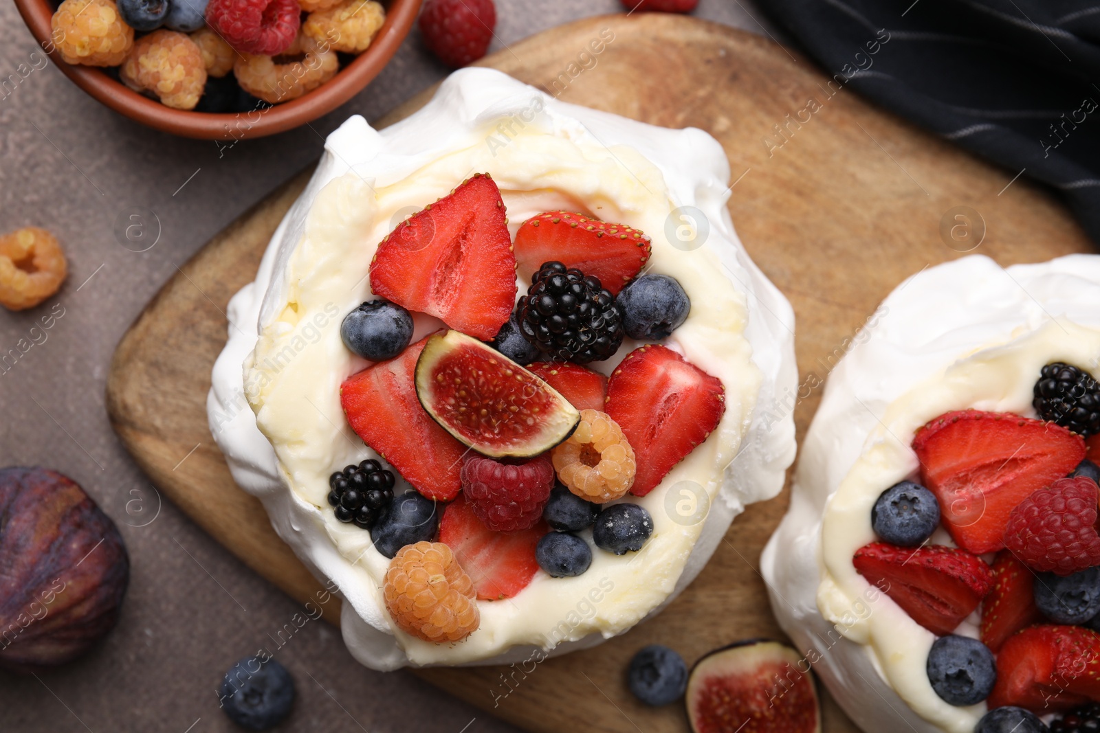 Photo of Pavlova cake (meringue dessert) with whipped cream, fresh berries and fig on brown table, flat lay