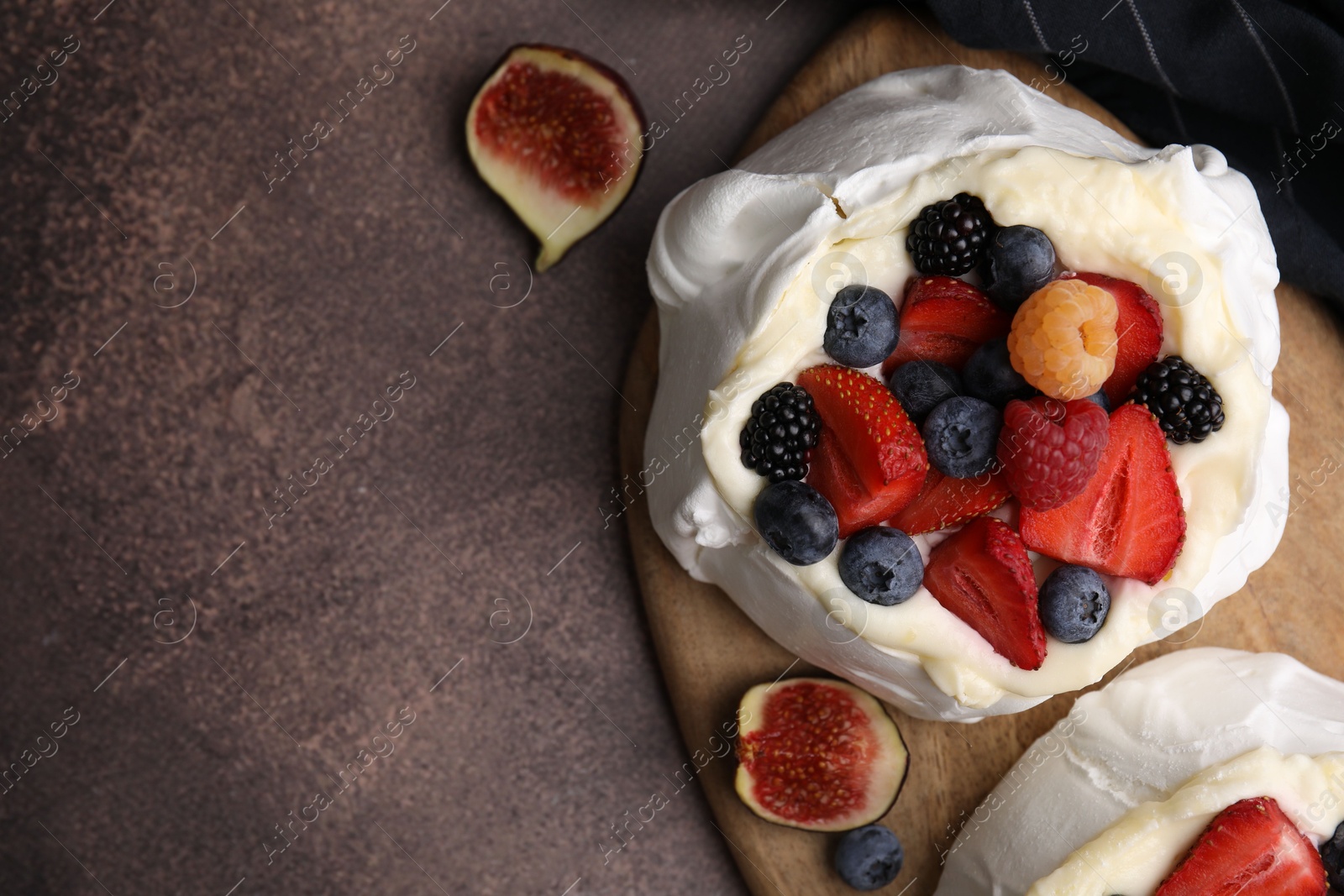 Photo of Pavlova cake (meringue dessert) with whipped cream, fresh berries and fig on brown table, top view. Space for text