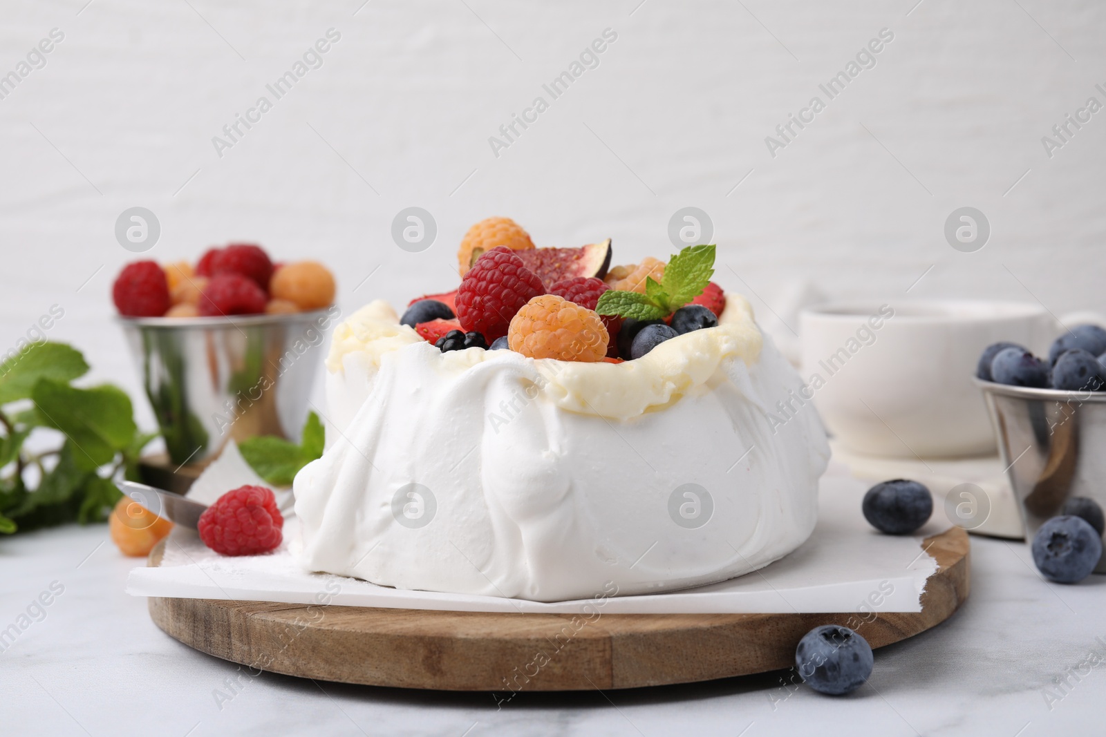 Photo of Pavlova cake (meringue dessert) with whipped cream, fresh berries and mint on white marble table, closeup